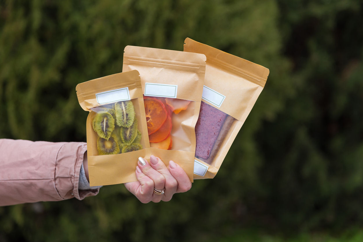 Dried fruits packaged in eco-friendly paper bags in hand. Pastila, persimmon and kiwi. Healthy desserts concept. Natural substitutes for sugar in the diet. Types of packaging materials